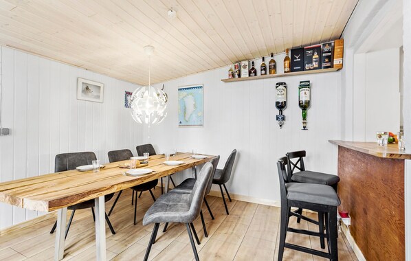 A dining area with a wooden table, grey upholstered chairs, and a bar area with liquor bottles and glasses.