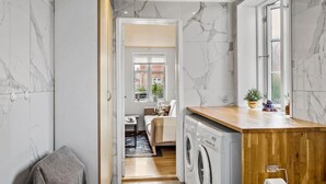 A compact laundry room with a washing machine, wooden counter, and a window. - Nice home in Nexø with WiFi (Nexø)