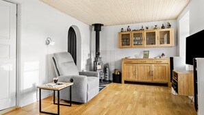 A modern living room with a grey armchair, a wooden coffee table, a fireplace, wooden cabinets, and a television. - Nice home in Nexø with WiFi (Nexø)