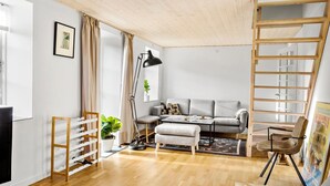 A modern living room with a grey sofa, wooden floor, and a ladder structure. - Nice home in Nexø with WiFi (Nexø)