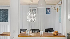 A dining area with a wooden table, chairs, a hanging light fixture, and a wall with a framed picture and a poster. - Nice home in Nexø with WiFi (Nexø)