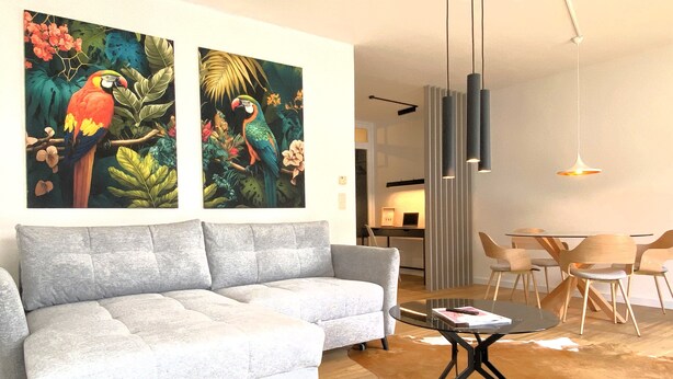 A living room with a grey sofa, a glass coffee table, and a dining area with wooden chairs and a glass table.