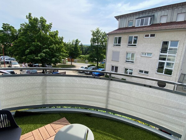 A modern building with a curved balcony, a parking area with cars, and a grassy lawn.