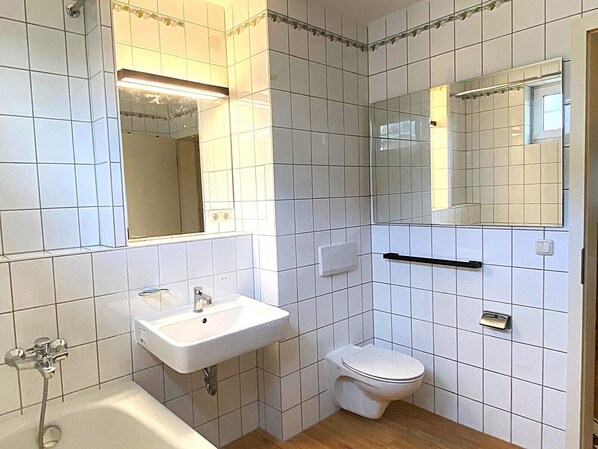 Un baño con azulejos blancos, un lavamanos, un inodoro y una ducha.