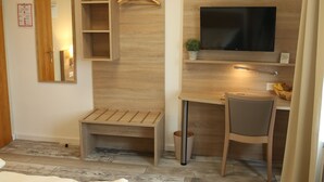 A hotel room with a bed, a desk with a chair, a TV, a mirror, and a small shelf with a plant. - smal-Apartment (Ostfildern)