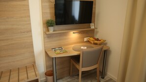 A compact room with a flat-screen TV mounted on the wall, a small table with a chair, a bowl of fruit, and a potted plant. - smal-Apartment (Ostfildern)