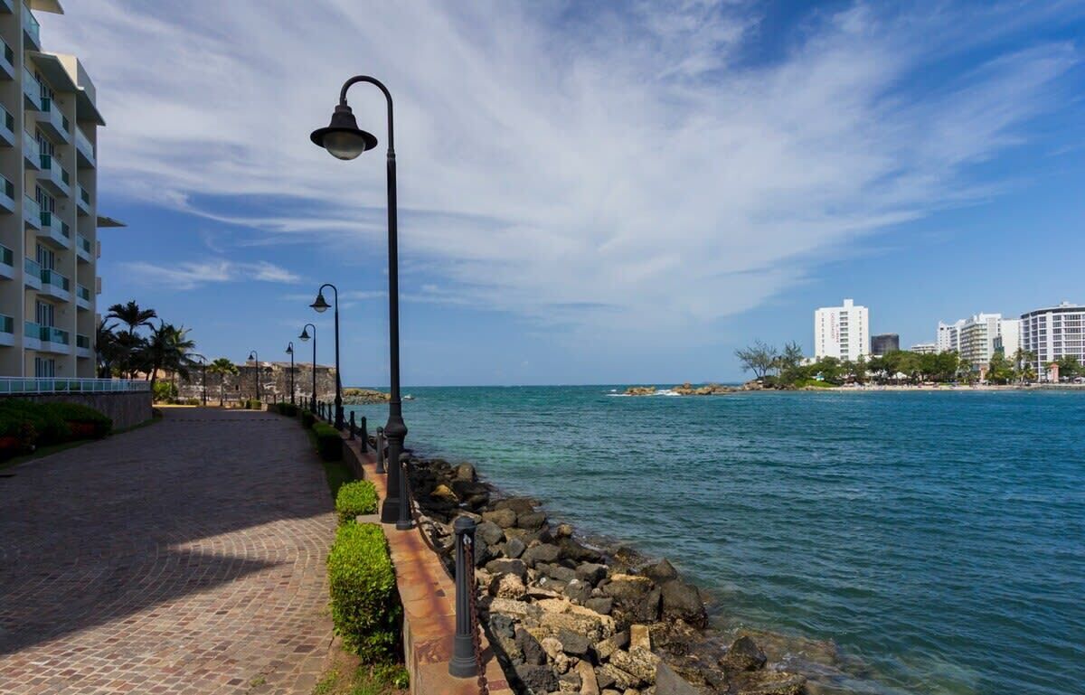 Une promenade en bord de mer, avec un chemin piétonnier pavé, des lampadaires et une côte rocheuse.