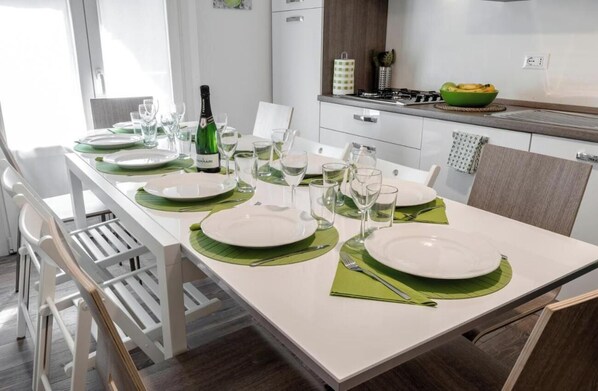 A dining area with a white table set for four, green placemats, and a bottle of wine.