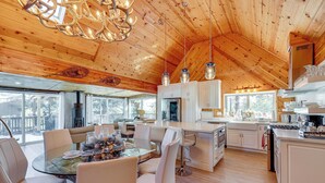 A spacious kitchen with wooden ceilings, a dining area with a glass table, and a view of the outdoors. - Wraparound Deck & Grill: Wrightwood Cabin Near PCT (Wrightwood)