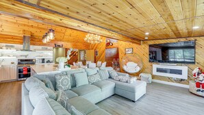 A spacious living area with a large sectional sofa, a kitchen with modern appliances, and a flat-screen TV mounted on the wall. - Wraparound Deck & Grill: Wrightwood Cabin Near PCT (Wrightwood)
