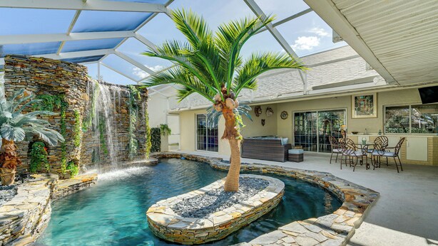 An indoor swimming pool with a waterfall, surrounded by stone walls and a palm tree. - 10 Mi to Beach: Pet-friendly Home in Punta Gorda! (Punta Gorda)