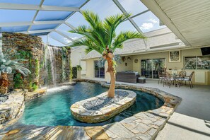 An indoor swimming pool with a waterfall, surrounded by stone walls and a palm tree. - 10 Mi to Beach: Pet-friendly Home in Punta Gorda! (Punta Gorda)