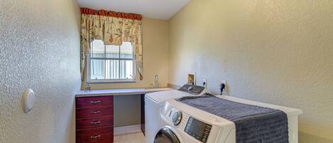 A compact laundry room with a washing machine, a dryer, a small sink, and a window with curtains.