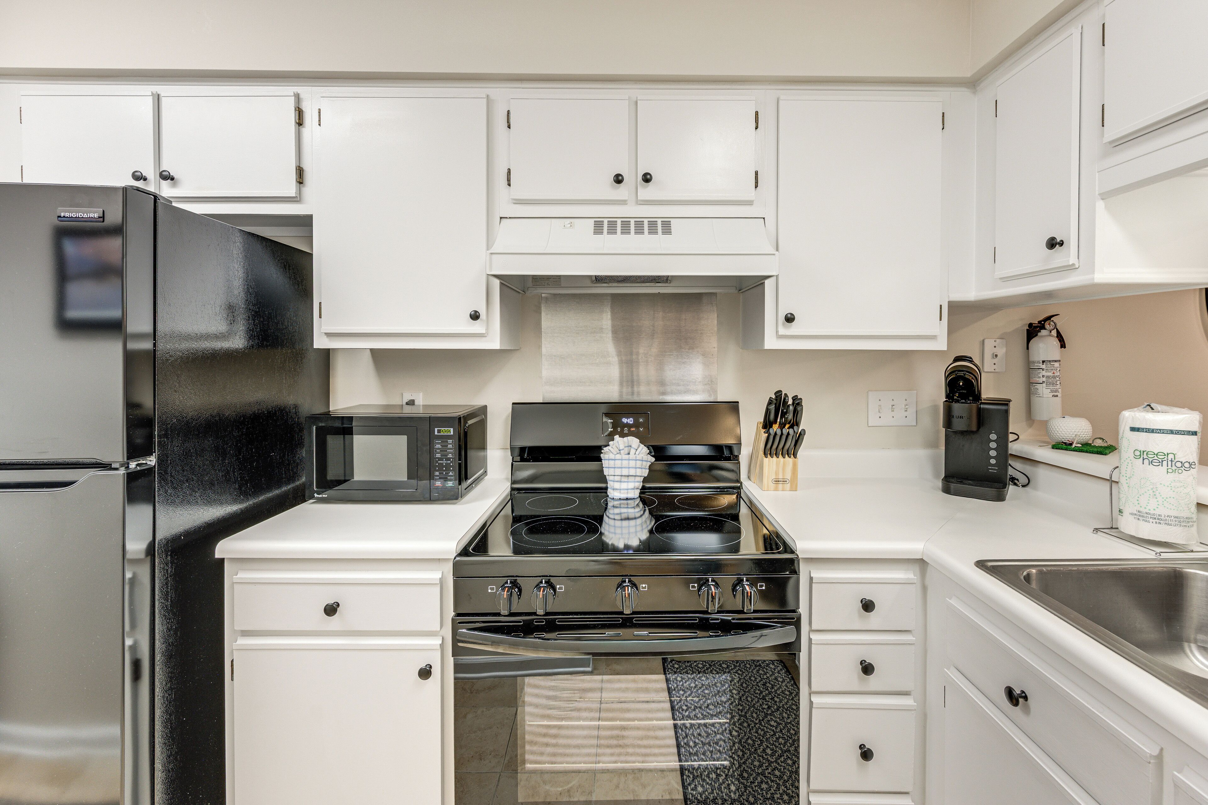 A kitchen with white cabinets, a stainless steel refrigerator, a microwave, a stove, and a coffee maker.