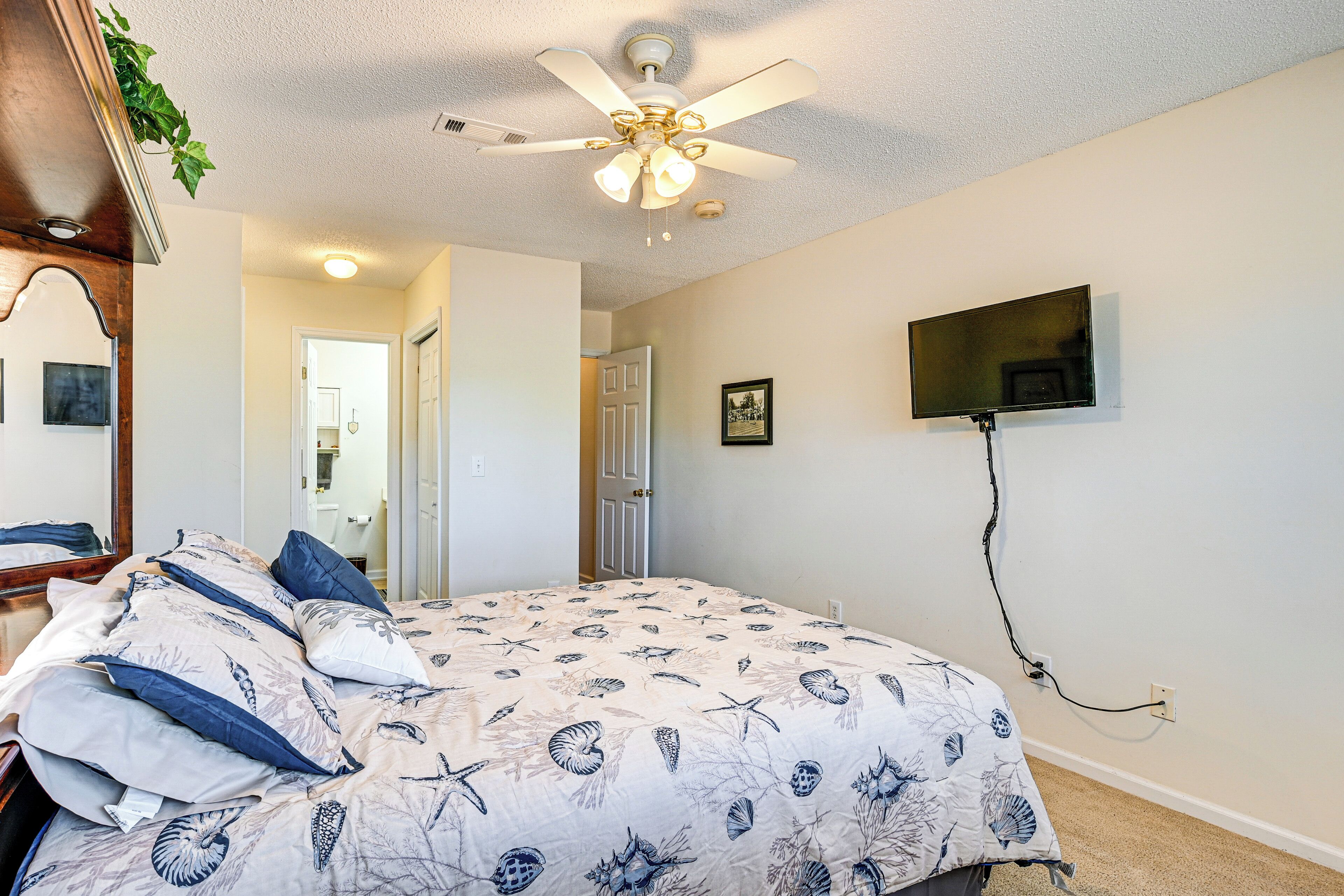 A bedroom with a bed, a ceiling fan, a TV mounted on the wall, and a door leading to another room.