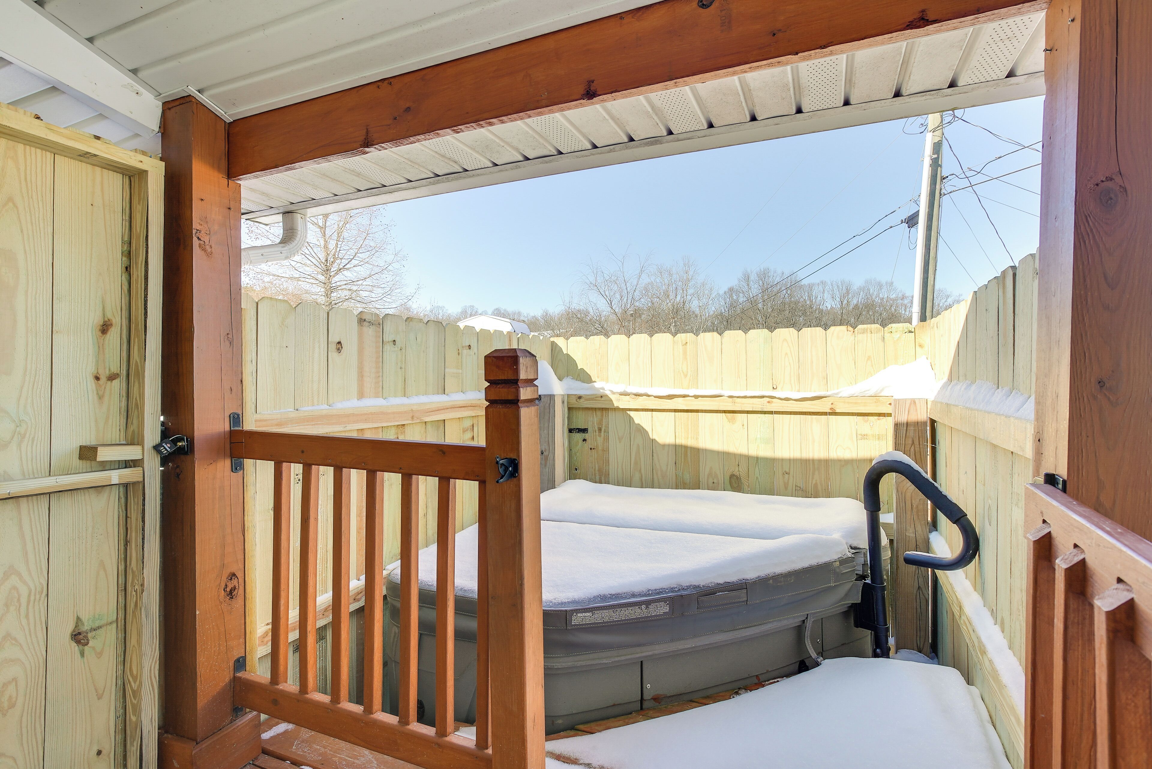 A wooden deck with a metal railing, a bench, and a mattress covered with a white sheet.