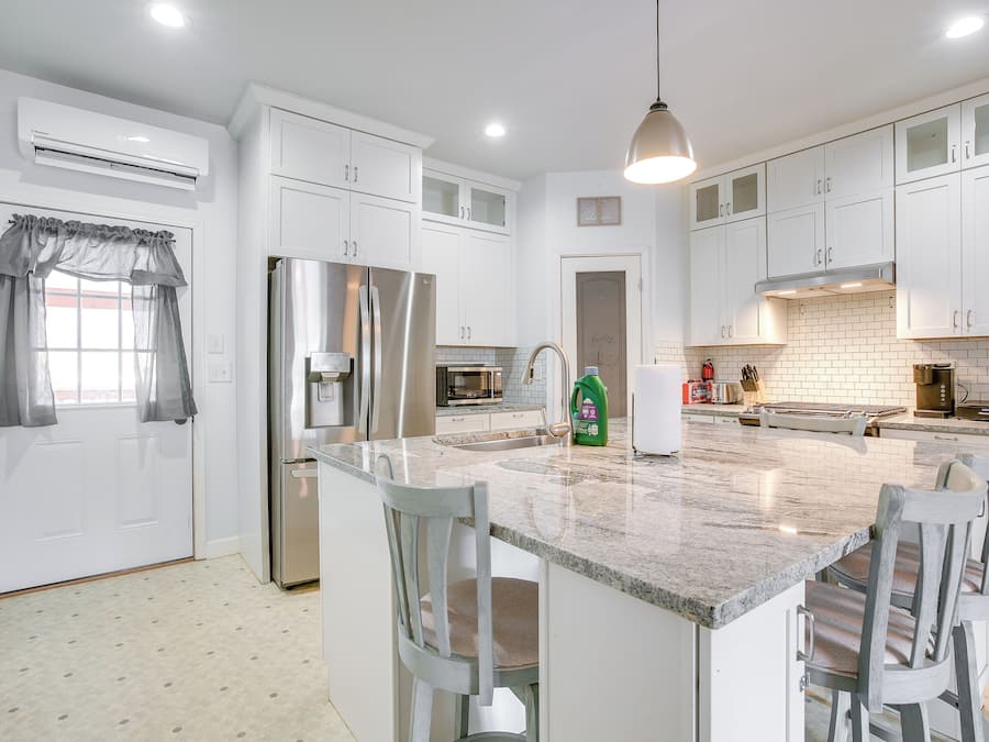 A modern kitchen with white cabinets, a stainless steel refrigerator, a granite countertop, and a built-in island with bar stools.