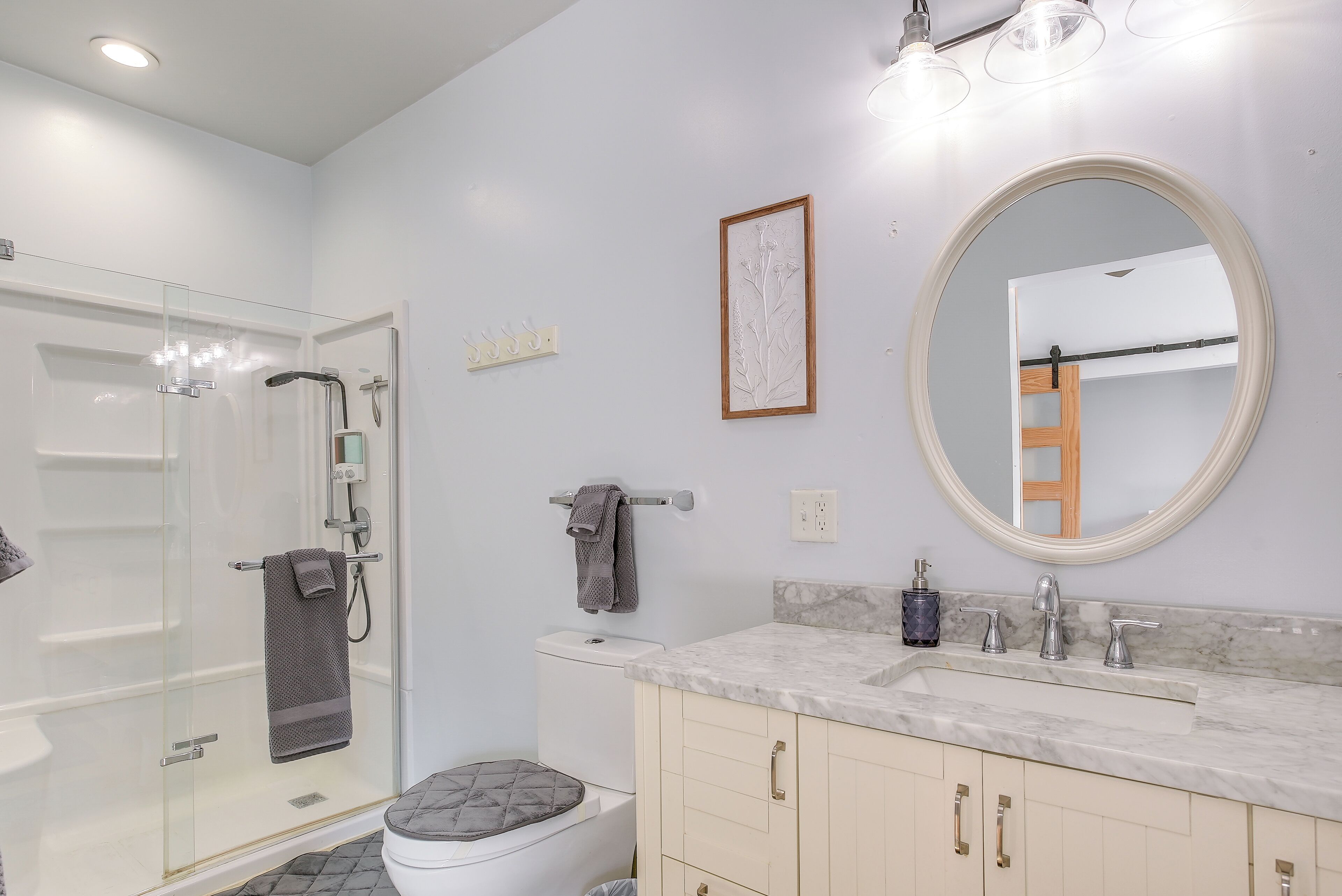 Une salle de bain moderne dotée d’une douche à parois de verre, de toilettes avec un porte-serviettes, d’un lavabo avec un plan de travail en marbre et d’un grand miroir.