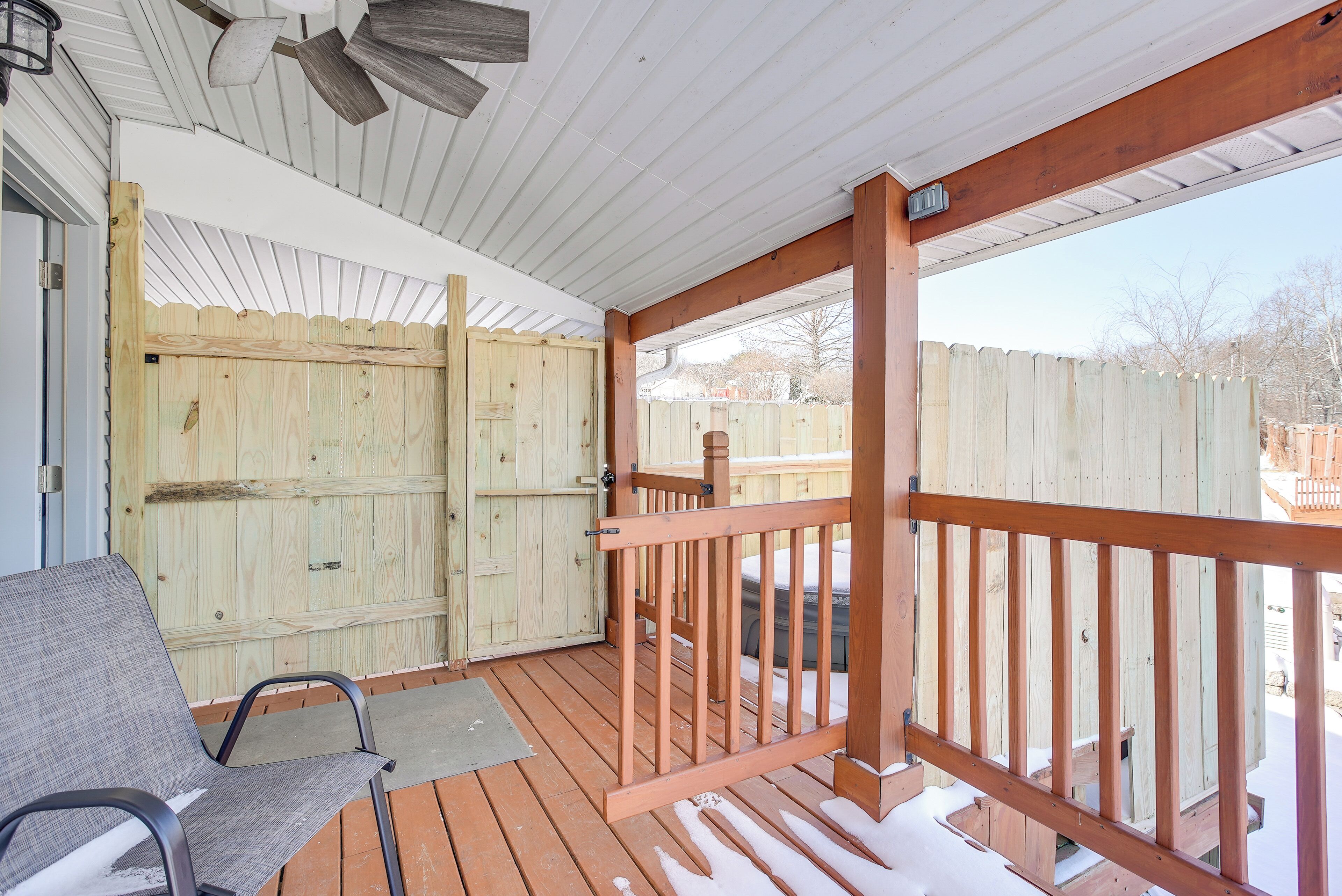 Une terrasse extérieure couverte, dotée d’une rambarde en bois, d’un banc et d’une clôture en bois en arrière-plan.
