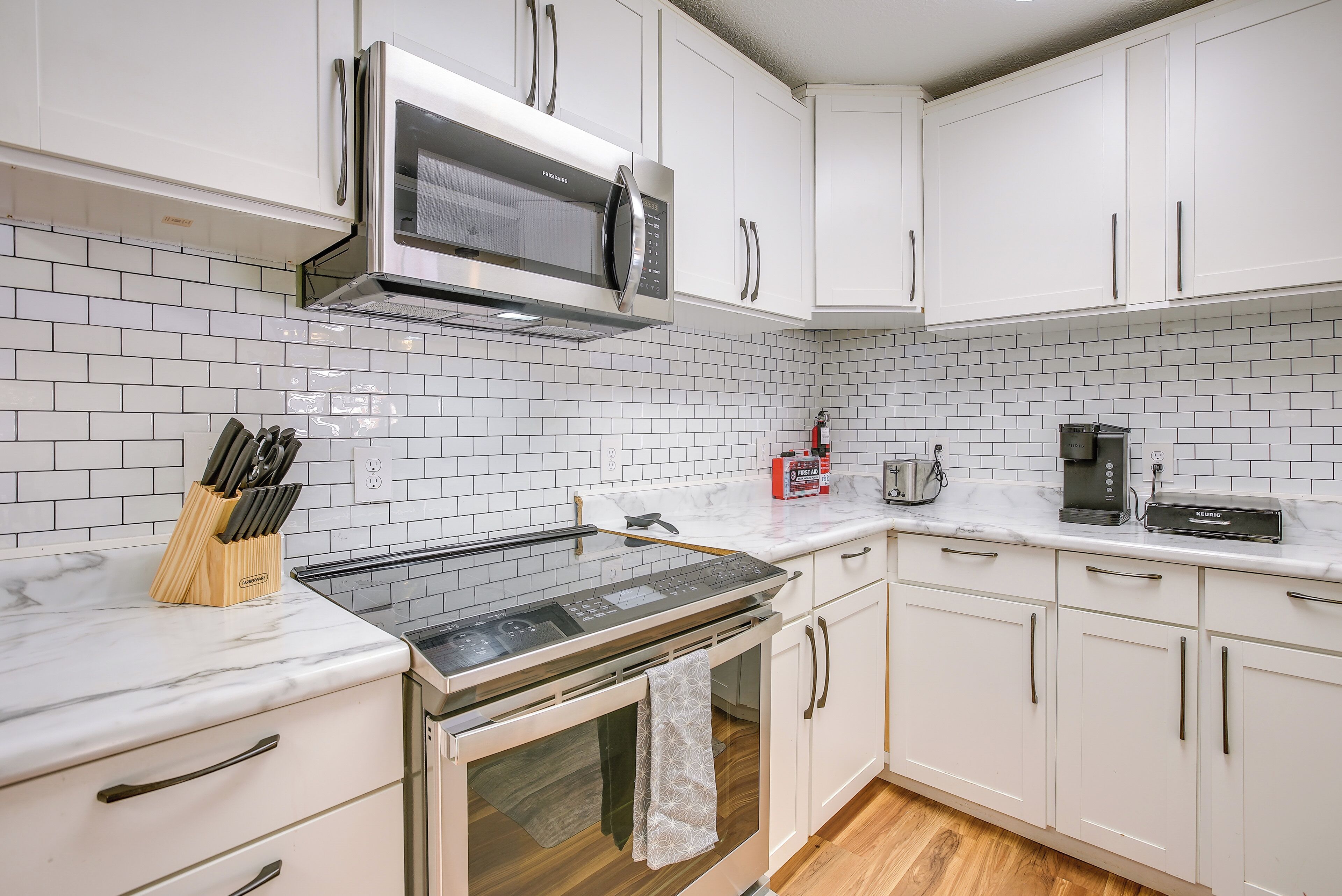 A modern kitchen with white cabinets, a microwave, a stove, and a coffee maker.