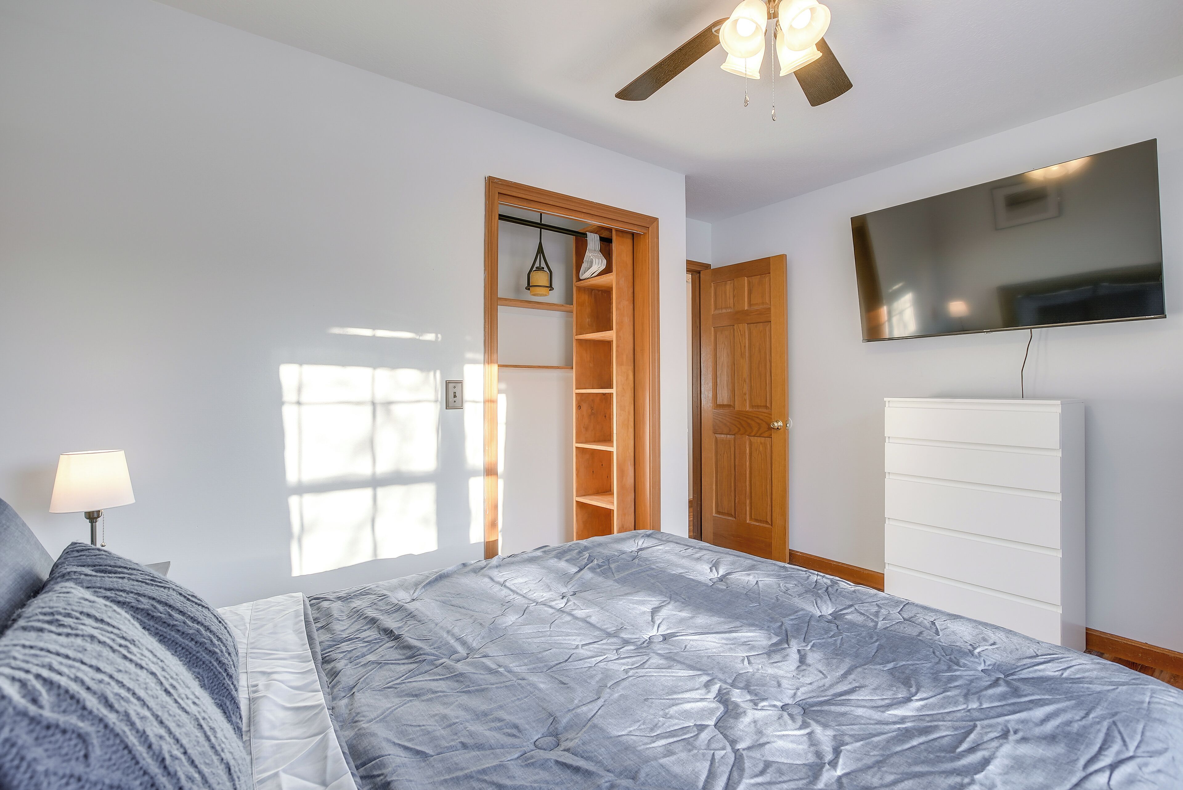 A bedroom with a bed, a wardrobe, a television, and a ceiling fan.