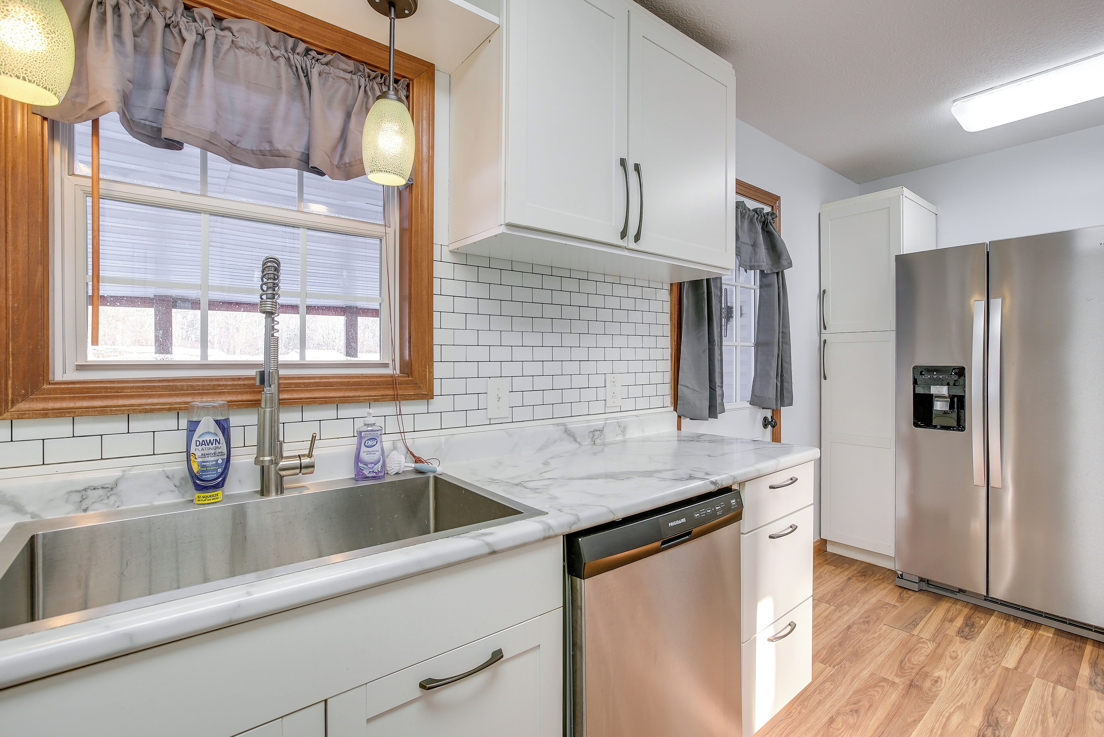 A kitchen with white cabinets, a stainless steel sink, a dishwasher, and a refrigerator.