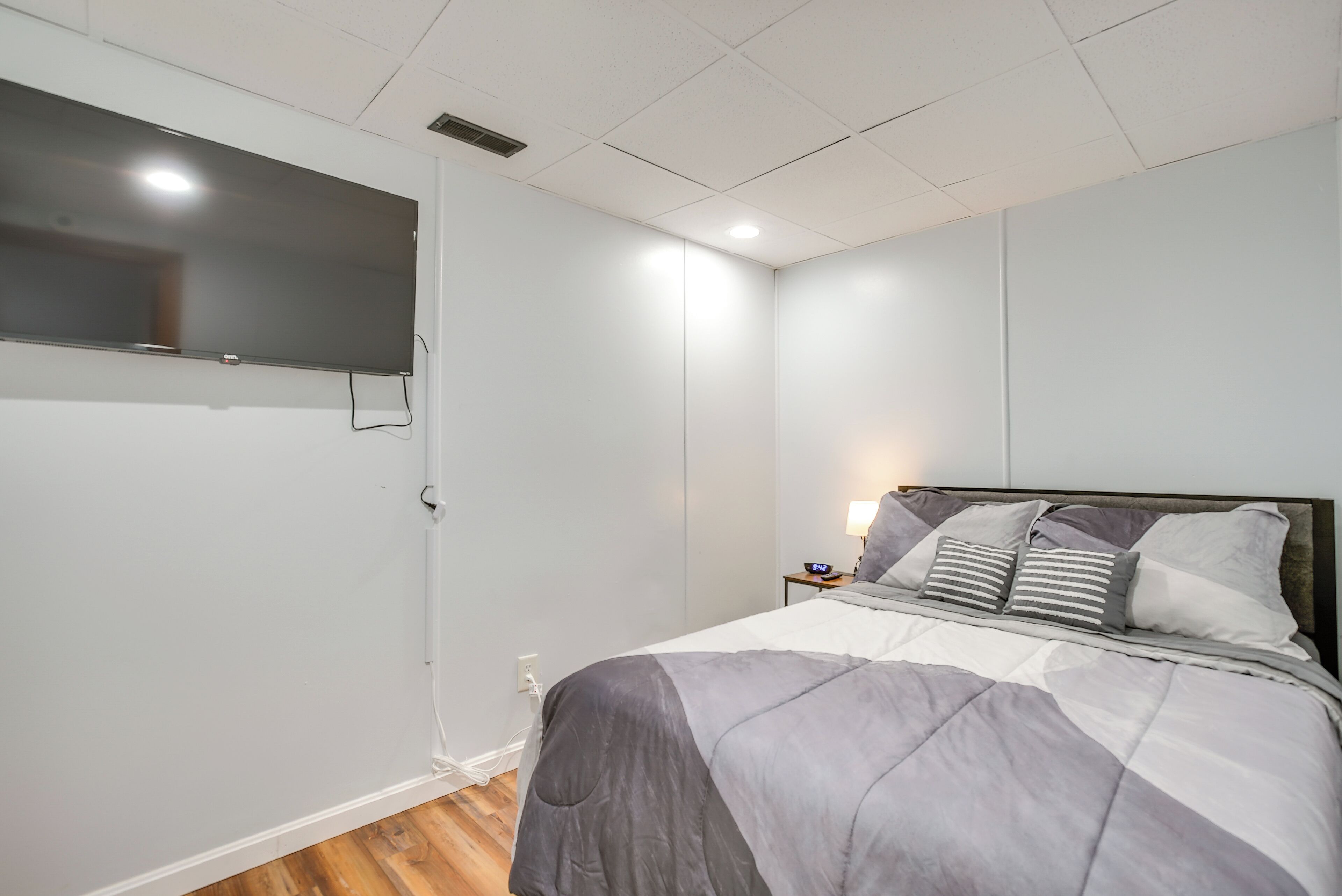 A bedroom with a bed, bedside table, lamp, and a flat-screen TV mounted on the wall.