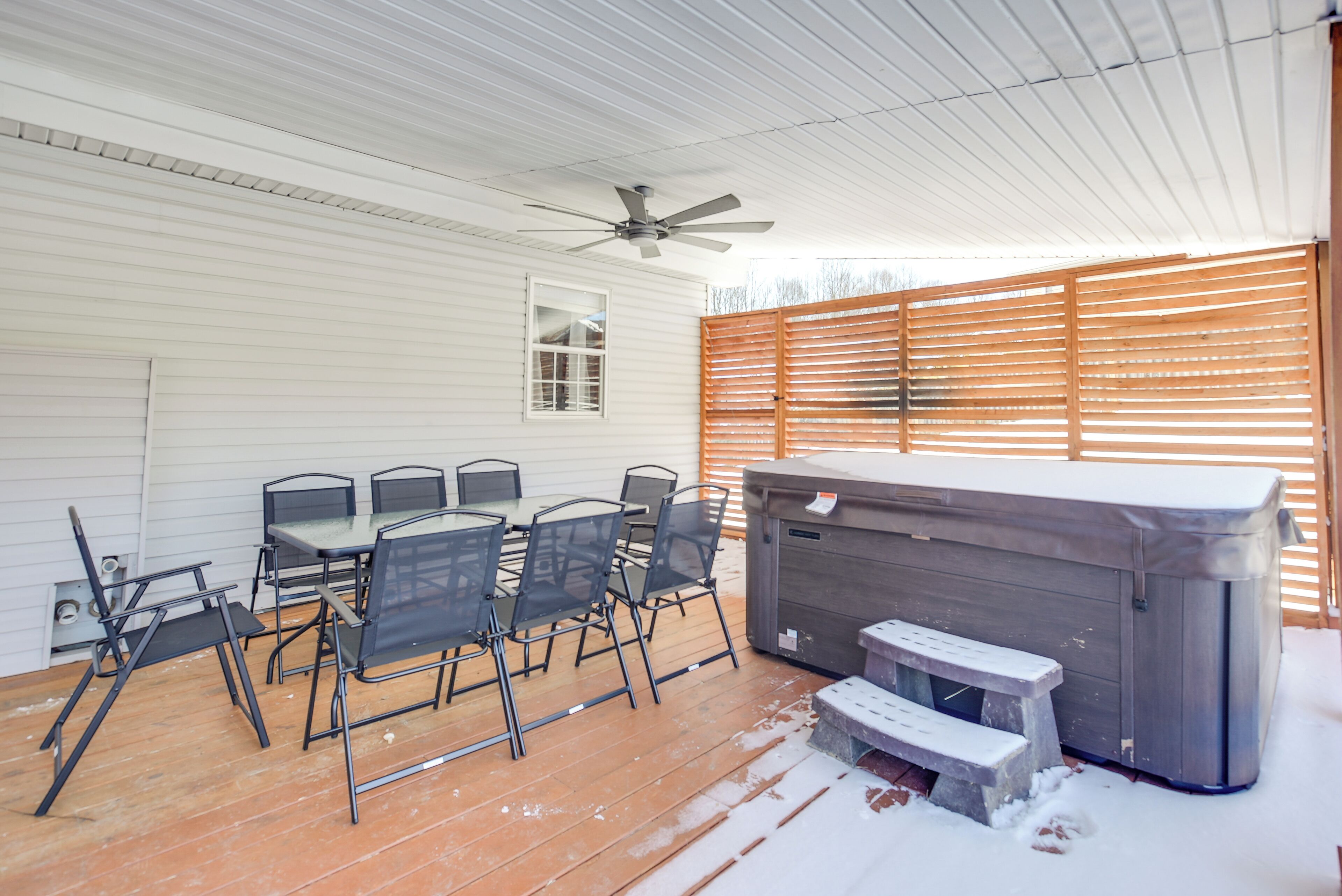 Eine überdachte Terrasse mit Tisch und Stühlen, einem Whirlpool und einem Deckenventilator.