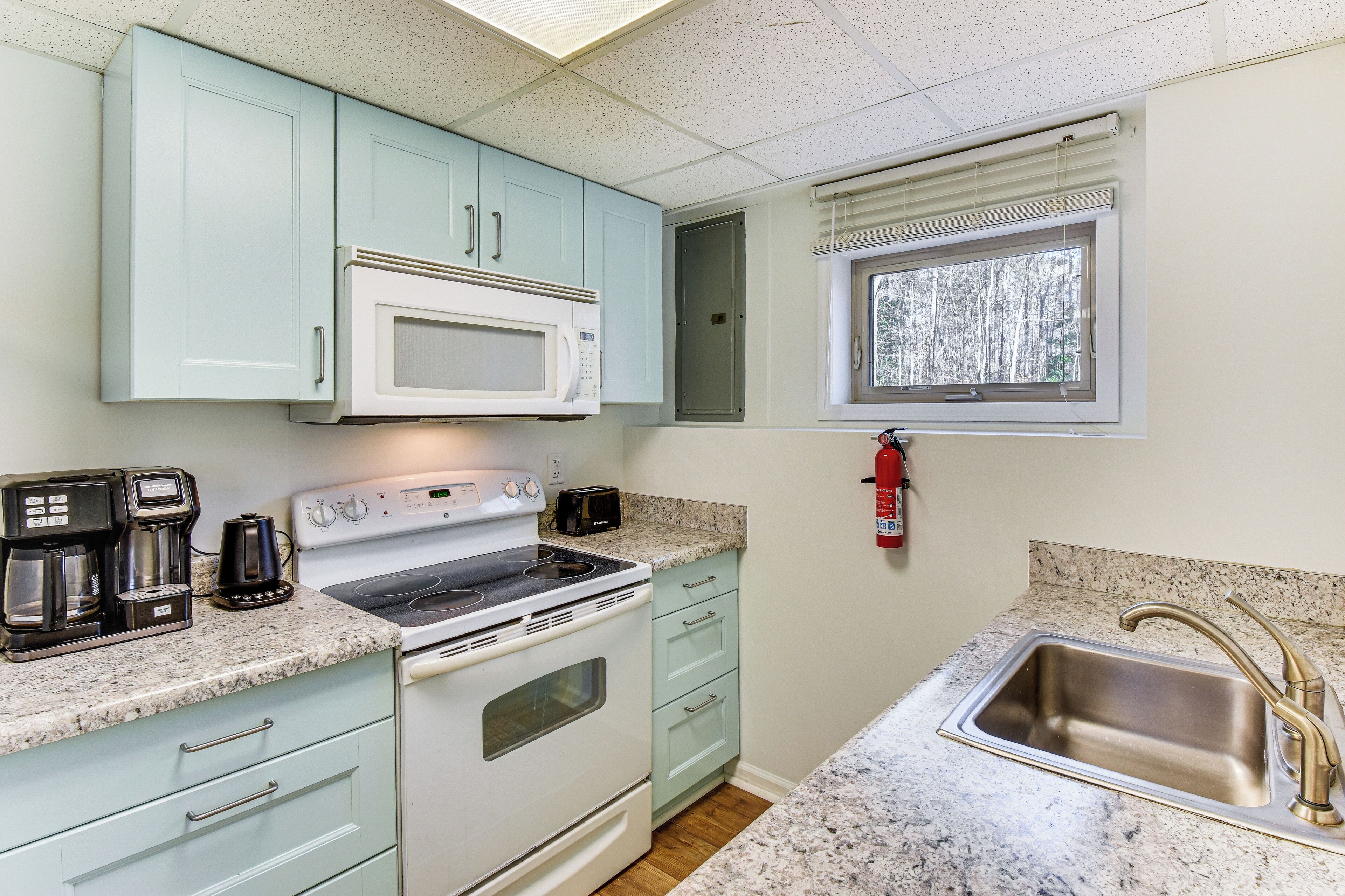 A compact kitchen with a white stove, a microwave, a coffee maker, and a sink with a faucet.