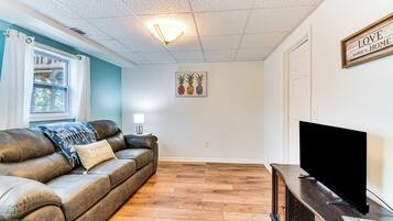 A living room with a leather sofa, a flat-screen TV on a wooden stand, and a wall with a 'LOVE makes a HOME' sign.