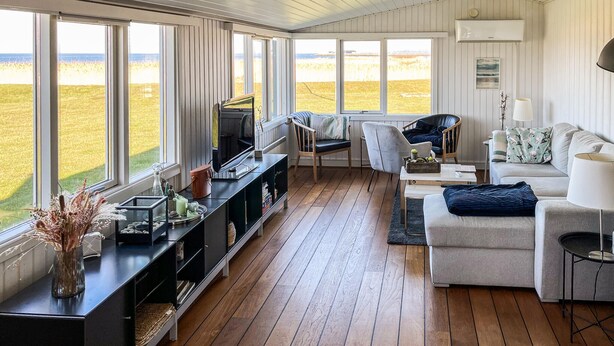 A spacious living room with a large window, wooden flooring, a sofa, a TV, and a bookshelf. - 2 bedroom stunning home in Vinderup (Vinderup)
