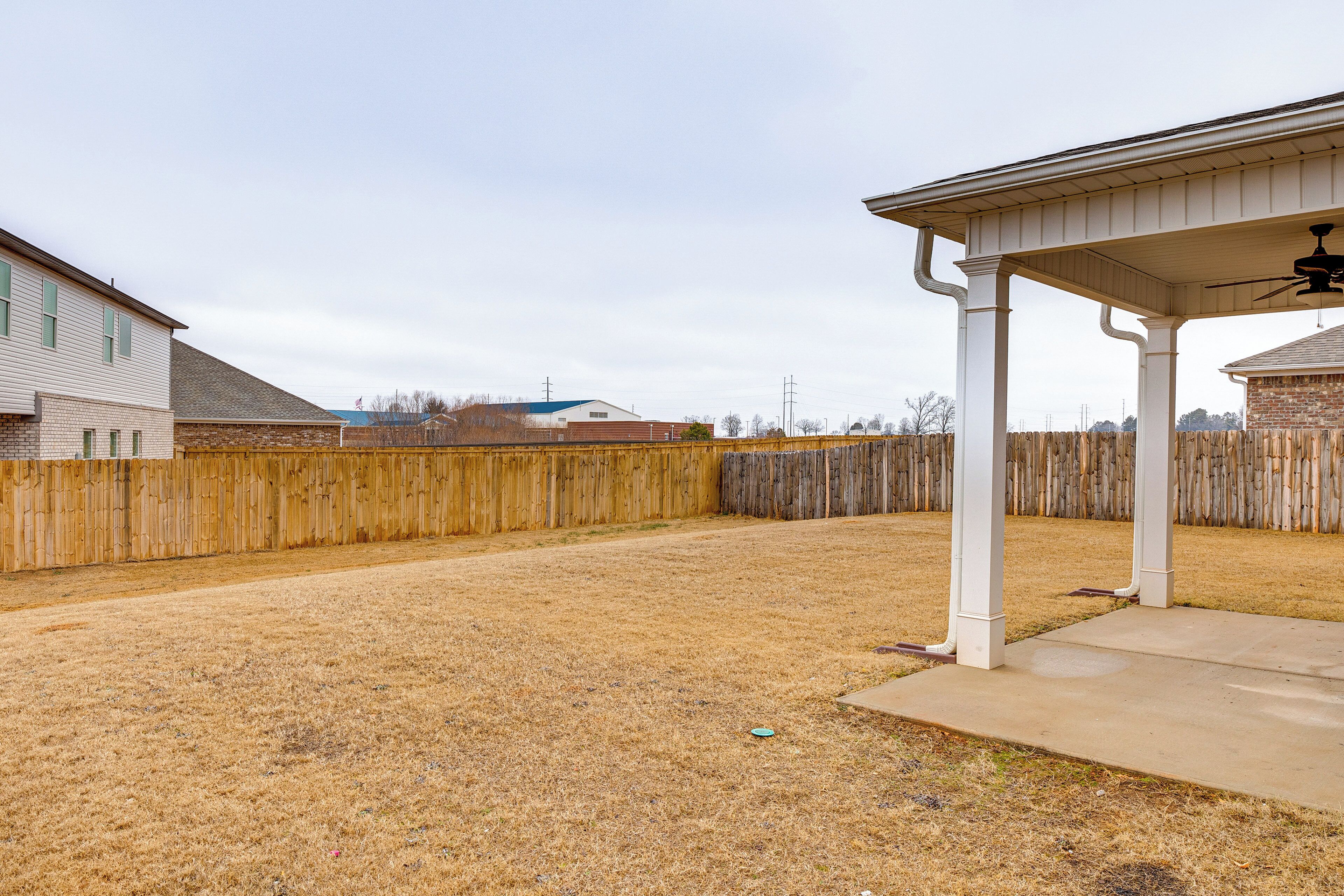 A backyard with a wooden fence, a covered patio area, and a concrete patio.