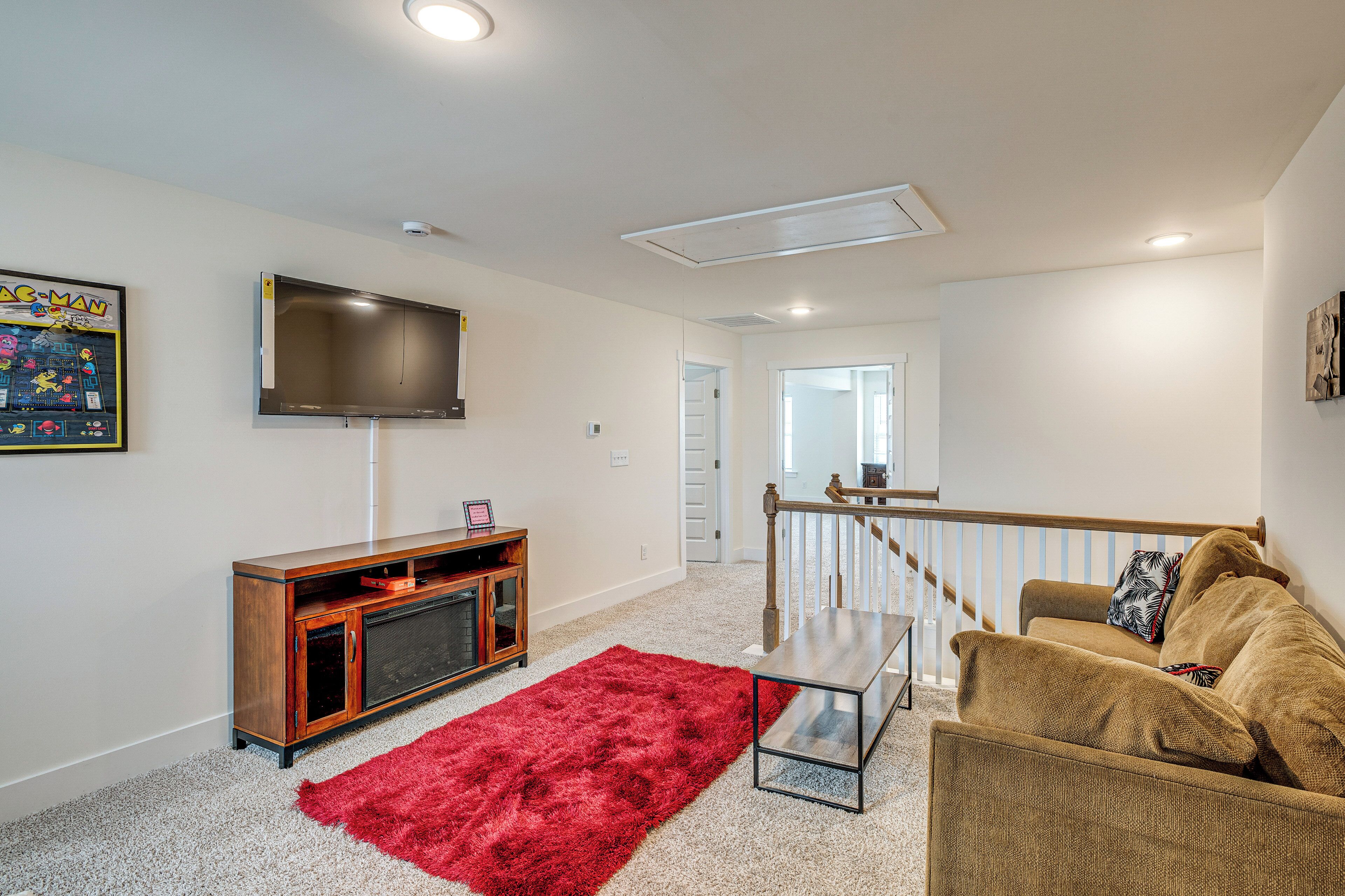 Una sala de estar con televisor, alfombra roja, mueble de entretenimiento de madera y sofá marrón.