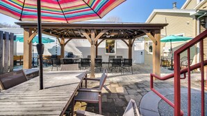 Ein überdachter Patio-Bereich mit Gartenmöbeln und einem gestreiften Sonnenschirm.