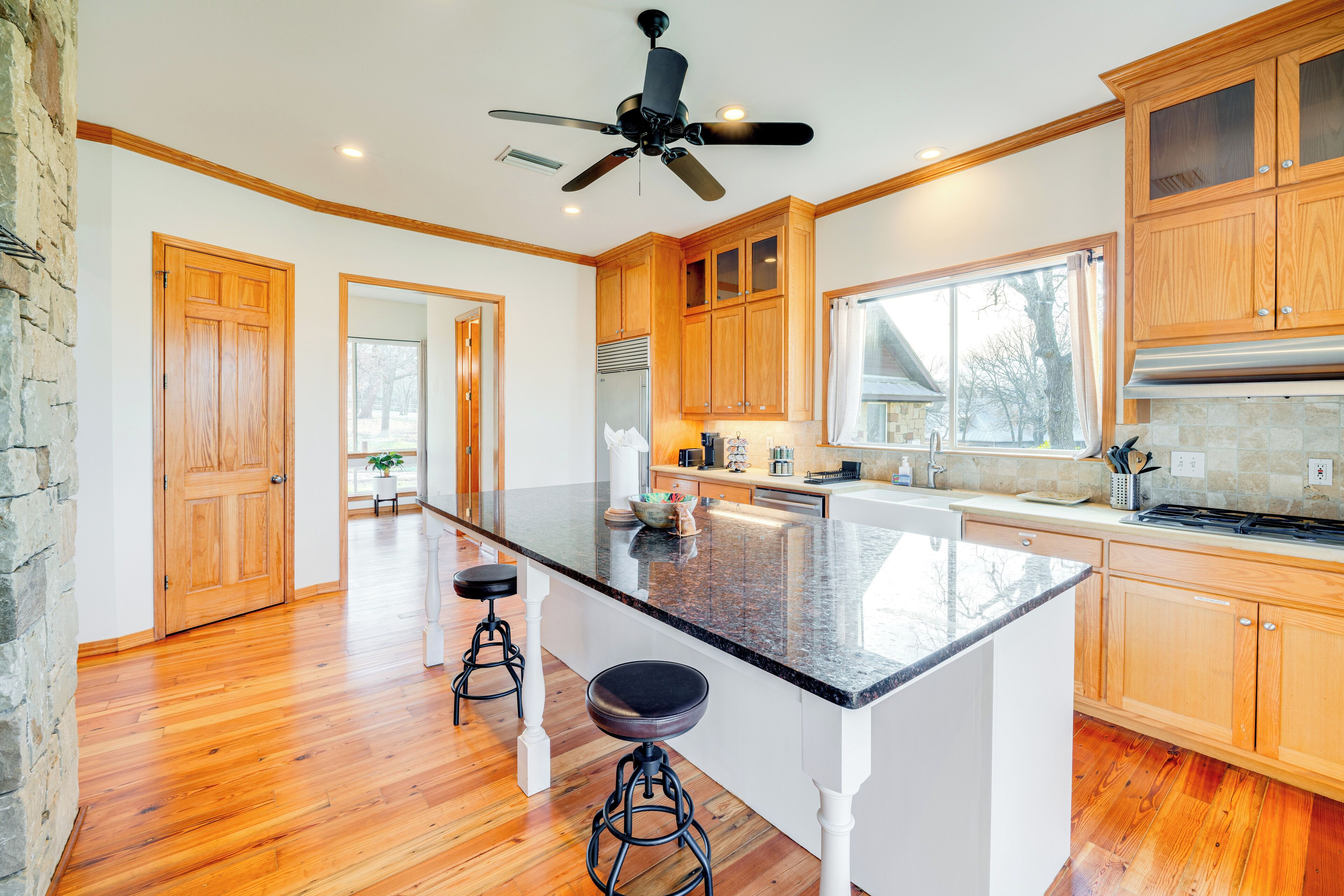 A spacious kitchen with wooden cabinets, a granite countertop, a central island with stools, and a ceiling fan.