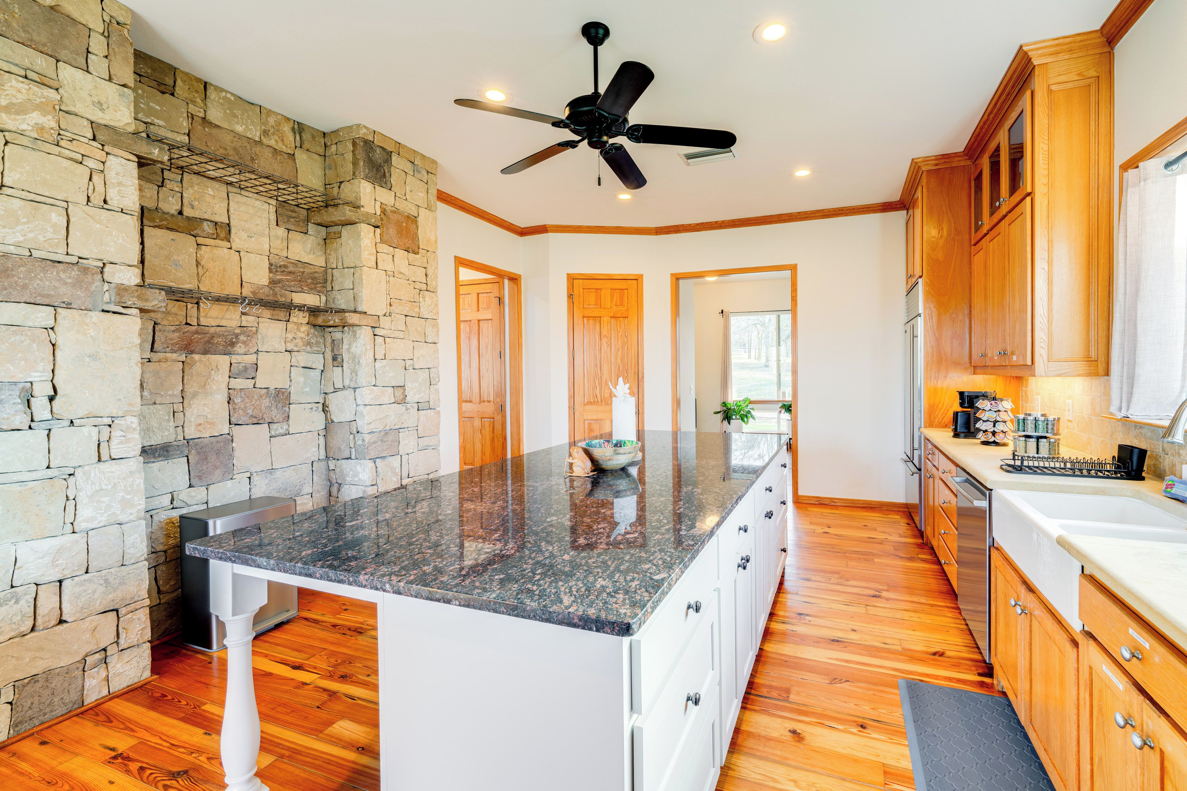 Una cocina con encimera de granito, armarios de madera, pared de piedra y ventilador de techo.