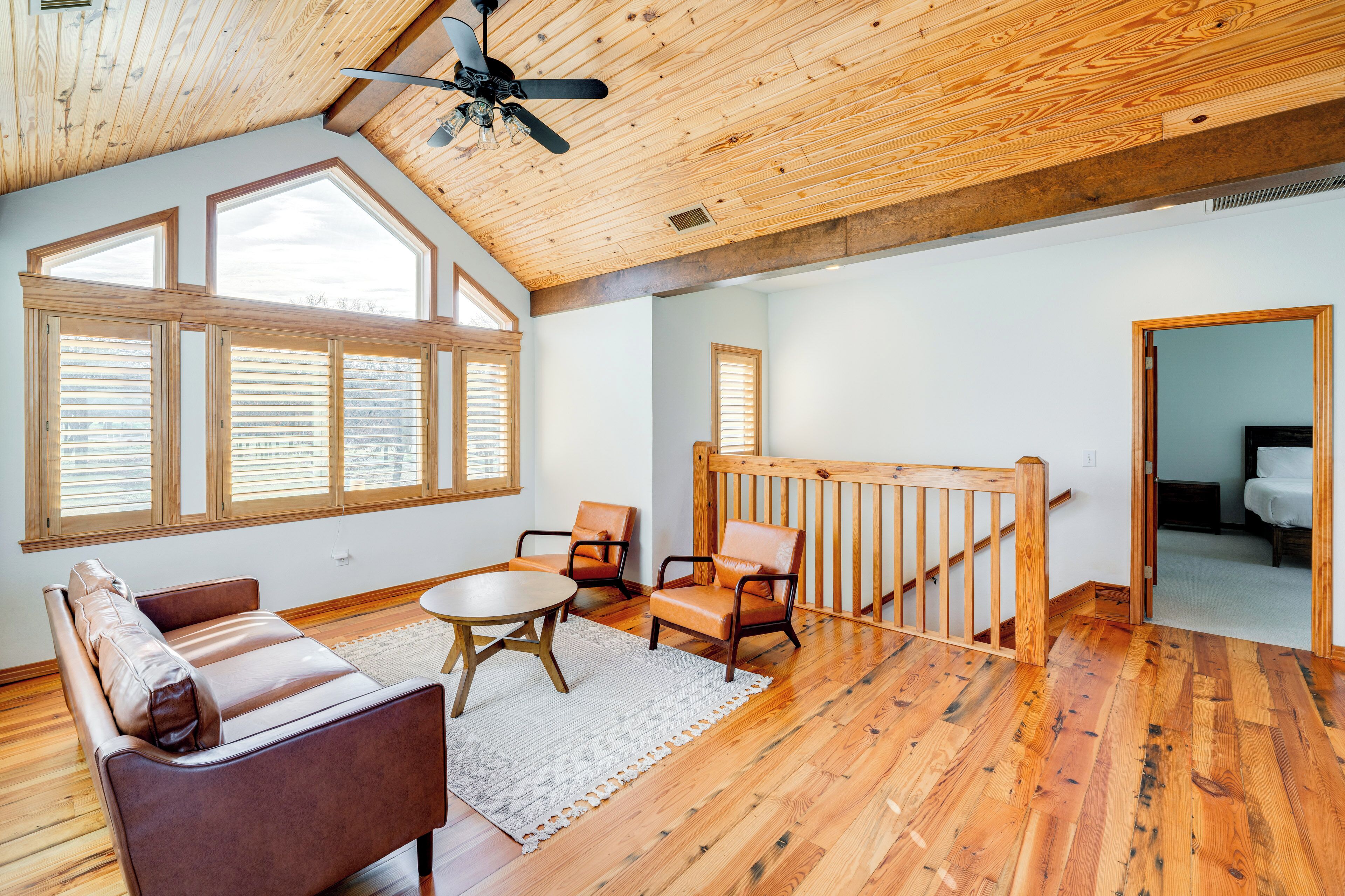 A spacious room with wooden flooring, a high ceiling, and large windows.