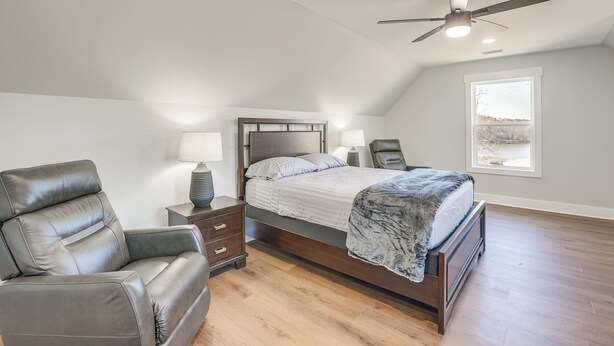 A bedroom with a bed, a leather chair, a nightstand, a ceiling fan, and a window with a view. - 7 Mi to Talladega Superspeedway: Home w/ Lake View (Lincoln)