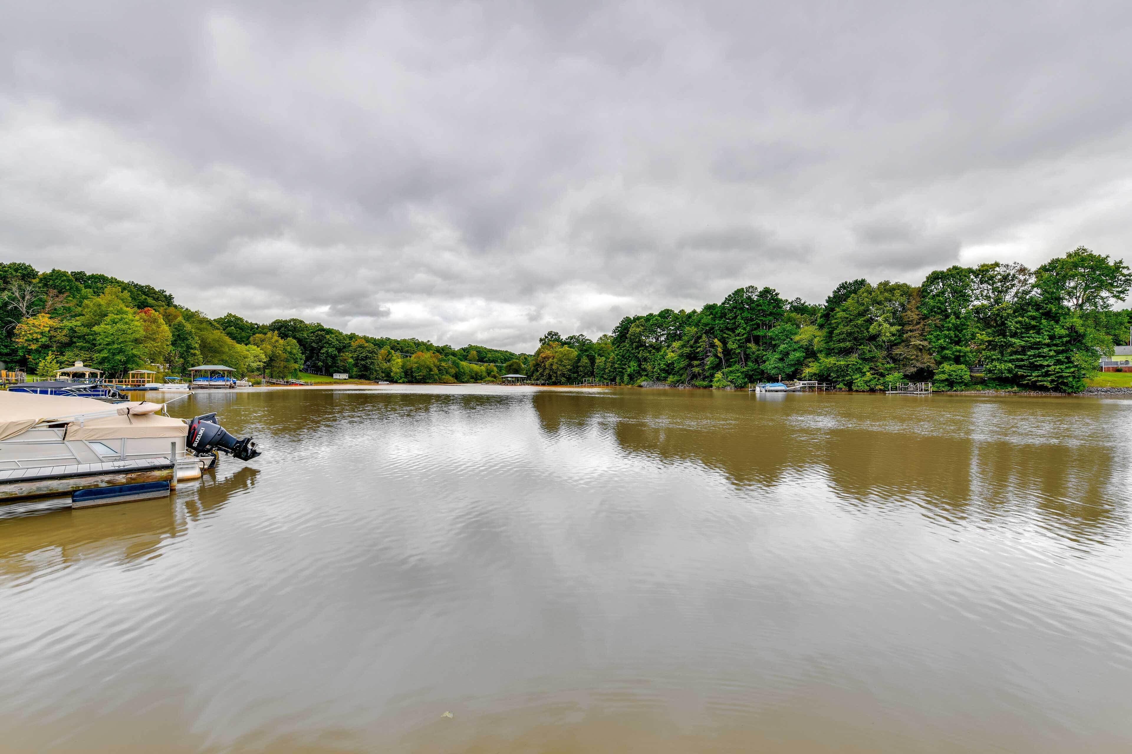 A calm lake with boats docked on the left, surrounded by dense trees and a cloudy sky.