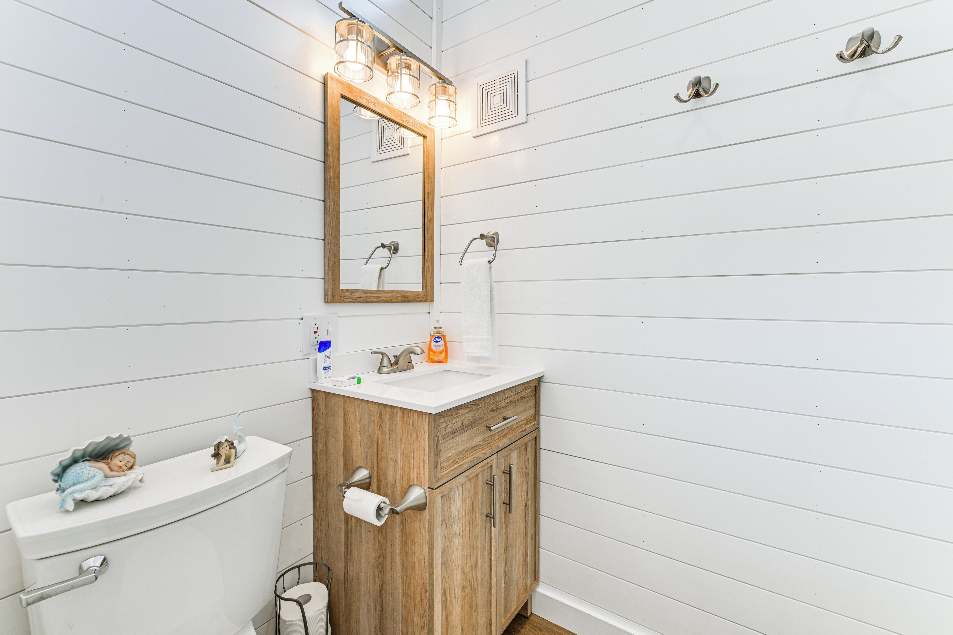 A bathroom with a wooden vanity, a white sink, a mirror with lights, and a toilet.