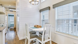 A dining area with a white table and chairs, a chandelier, and large windows with blinds. - Community Perks + Views: Cozy Lake Norman Cottage (Sherrills Ford)