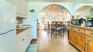 Una cocina con armarios blancos, una mesa de comedor de madera y sillas. Hay un refrigerador, una cafetera y un microondas en la encimera.