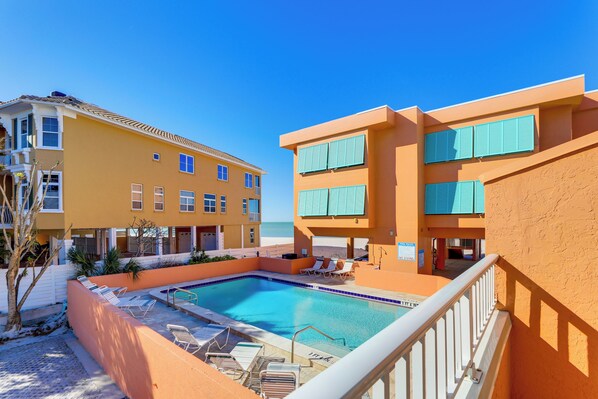 A pool area with lounge chairs and a clear view of the ocean.