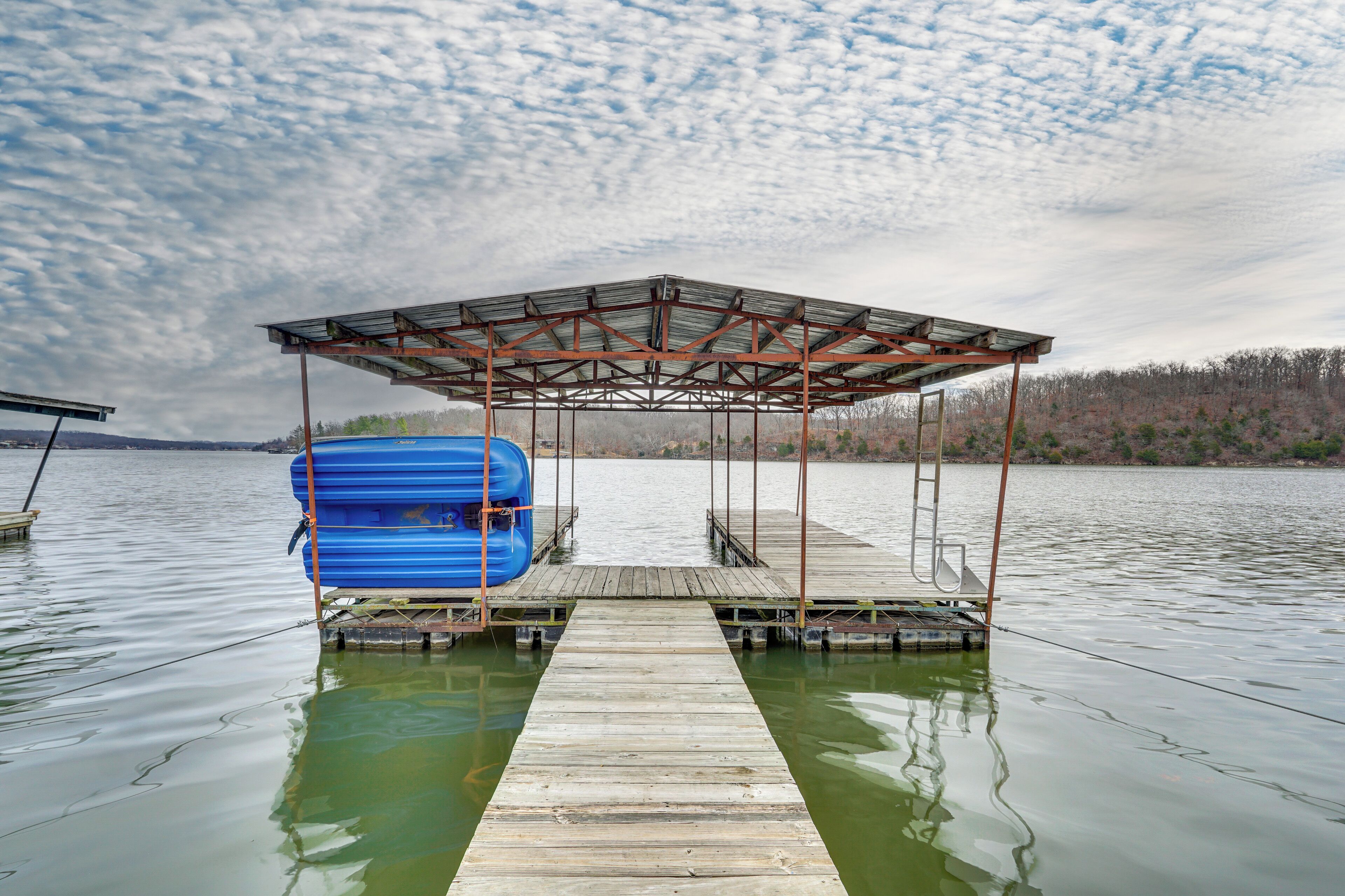 Une jetée en bois s’avançant dans un lac, avec une zone abritée et des kayaks bleus entreposés en dessous.