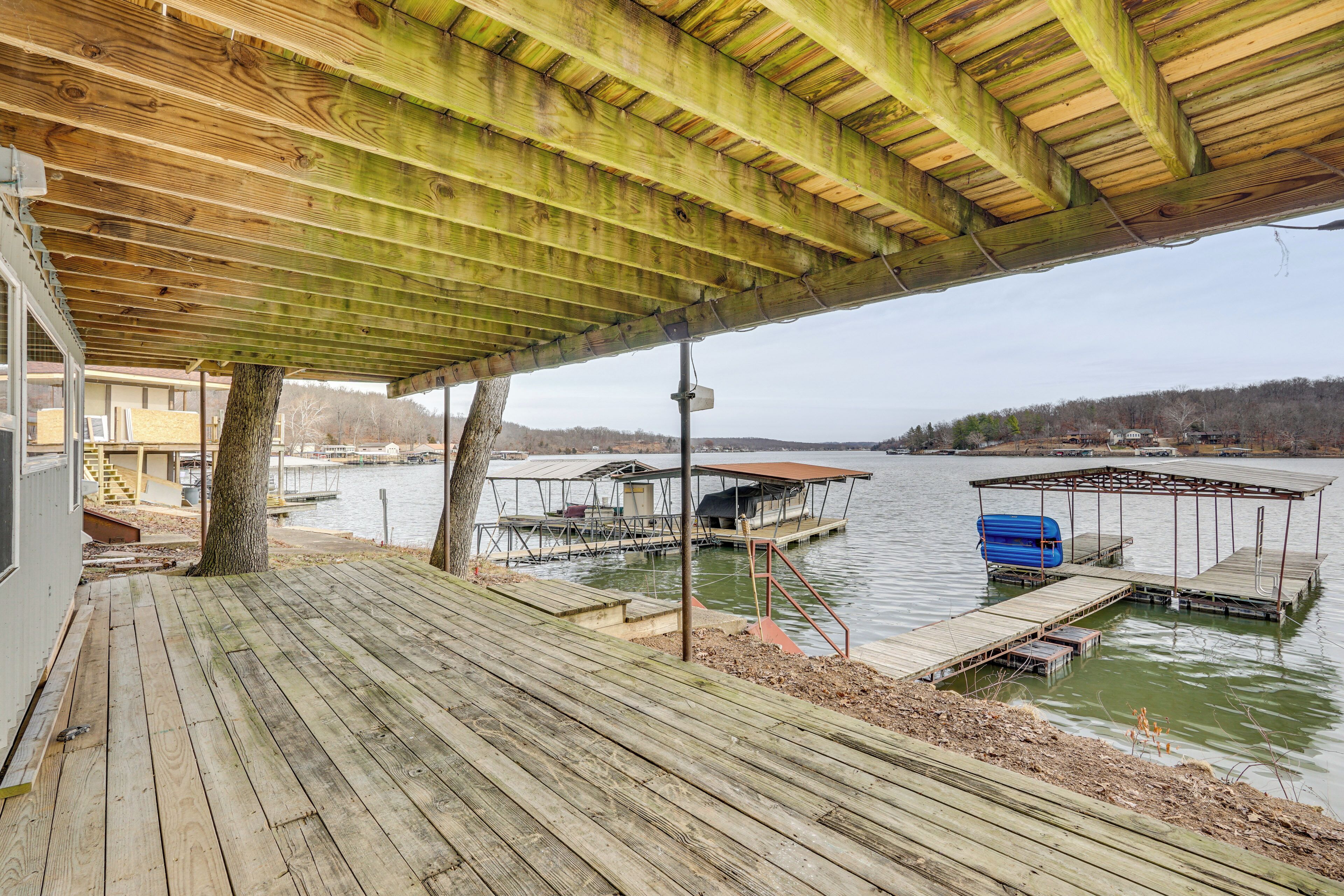 A wooden deck with a covered area overlooking a lake, docks, and a boat house.