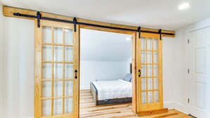 Une chambre avec un plancher en bois, un lit avec une literie blanche et une porte coulissante à panneaux de verre.