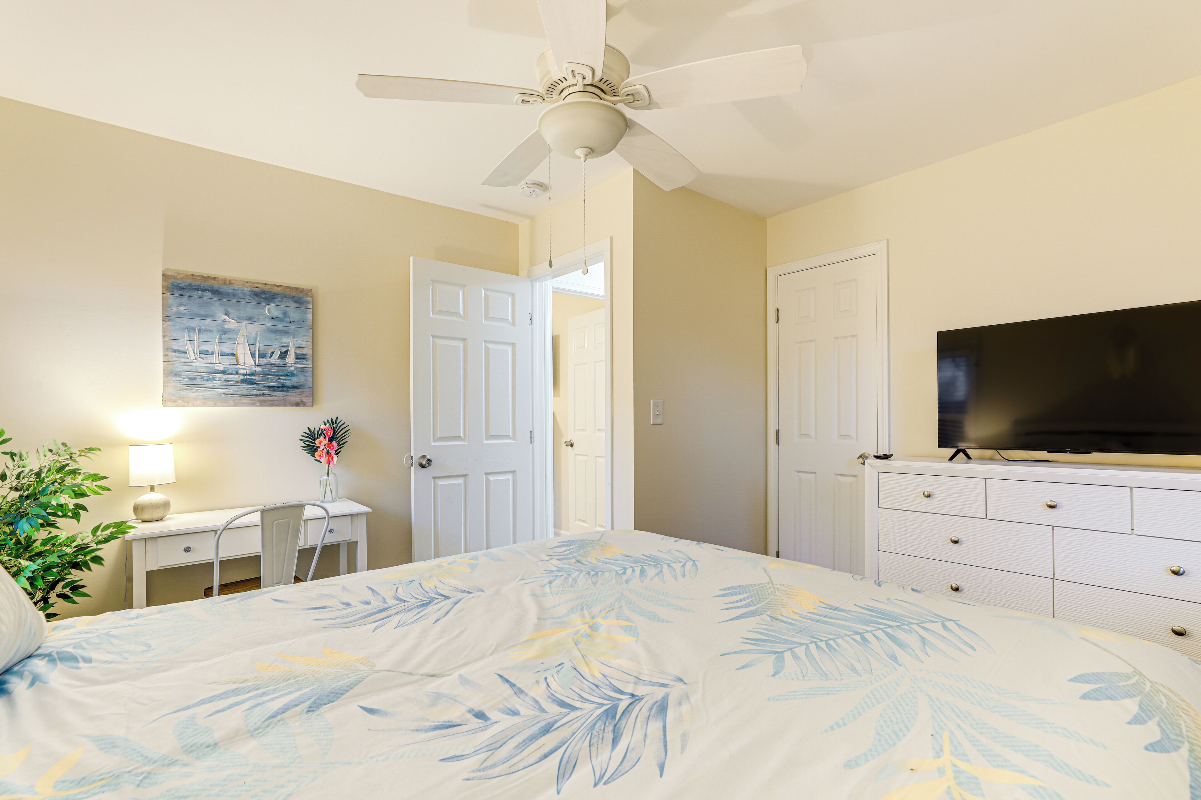 A bedroom with a bed, a desk, a chair, a television, and a ceiling fan.