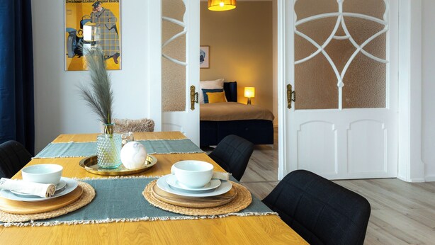 Een eetruimte met een houten tafel voor vier personen, een vaas met veren en een poster aan de muur.