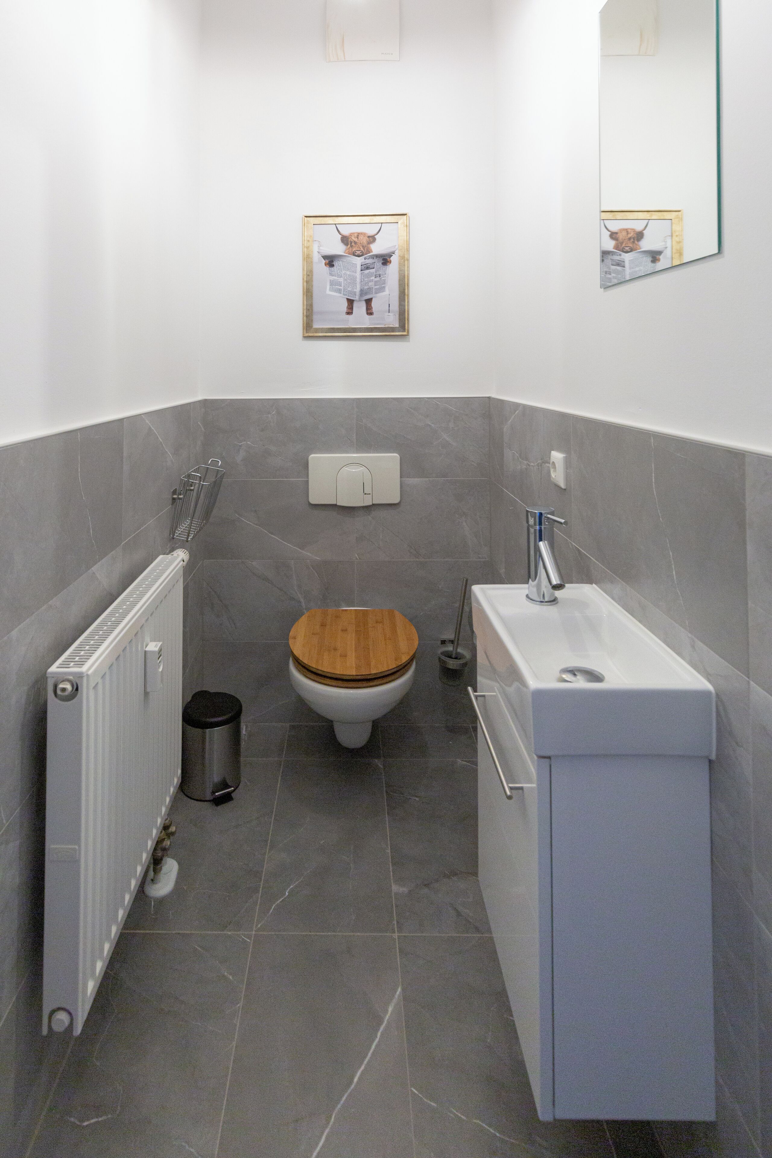 A modern bathroom with a wooden toilet, a white sink, and a mirror.