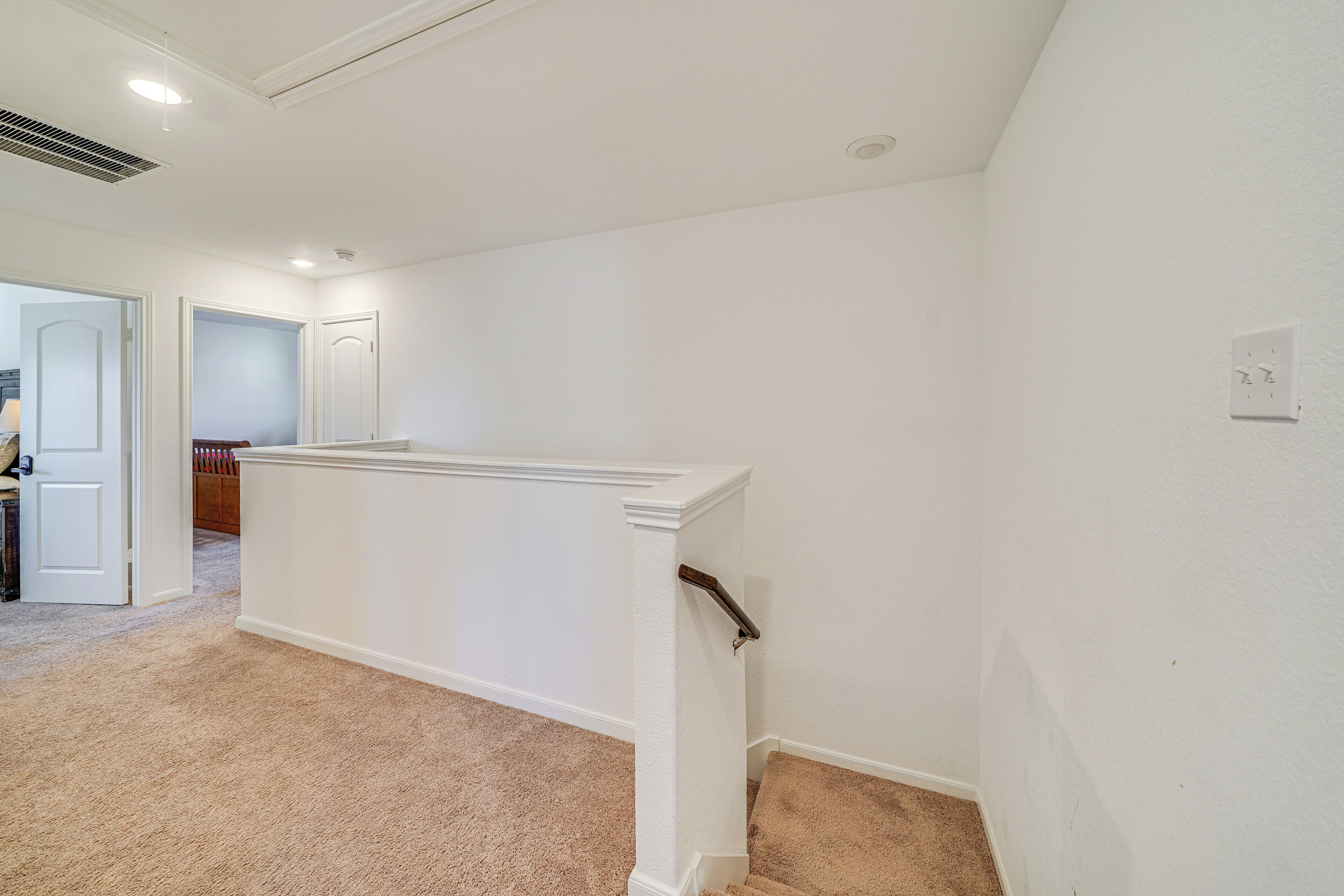 A hallway with a carpeted floor, white walls, and a door leading to another room.